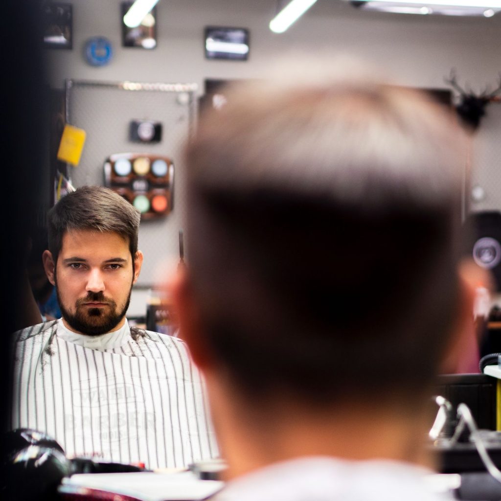 A man looking at his reflection in the mirror at a barbería cerca de mí.