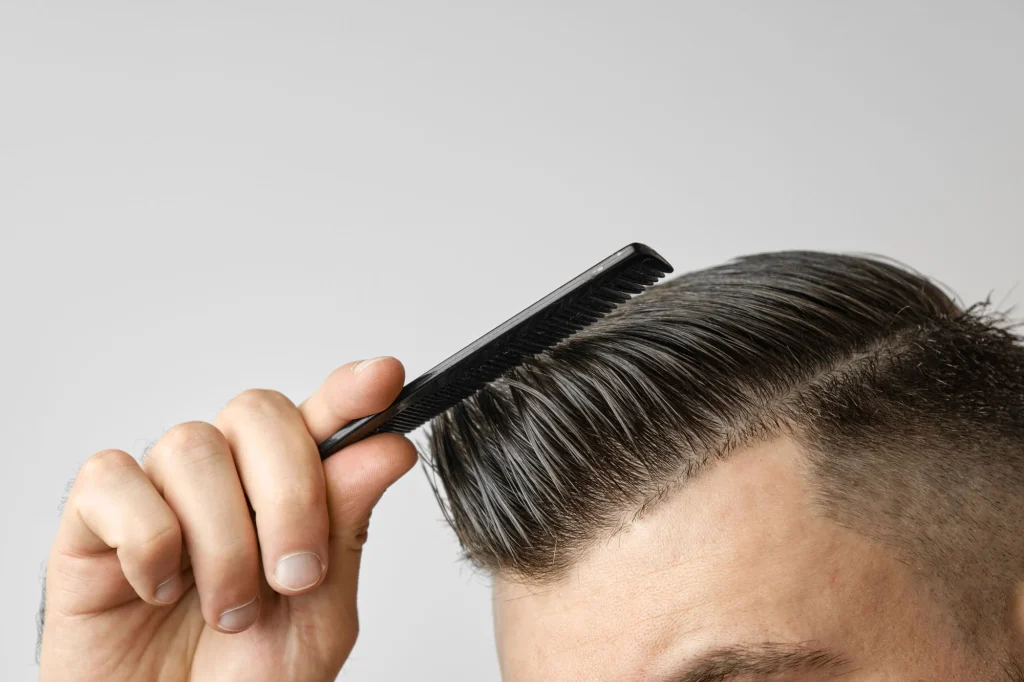 A hand combing a stylish mens haircut with a black comb, showcasing a sleek grooming style.
