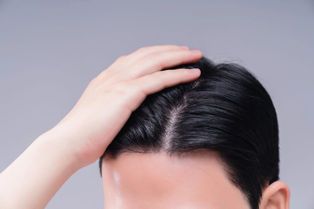 A hand touching a man's hair with a mens toupee in Stafford, highlighting natural hair replacement solutions.