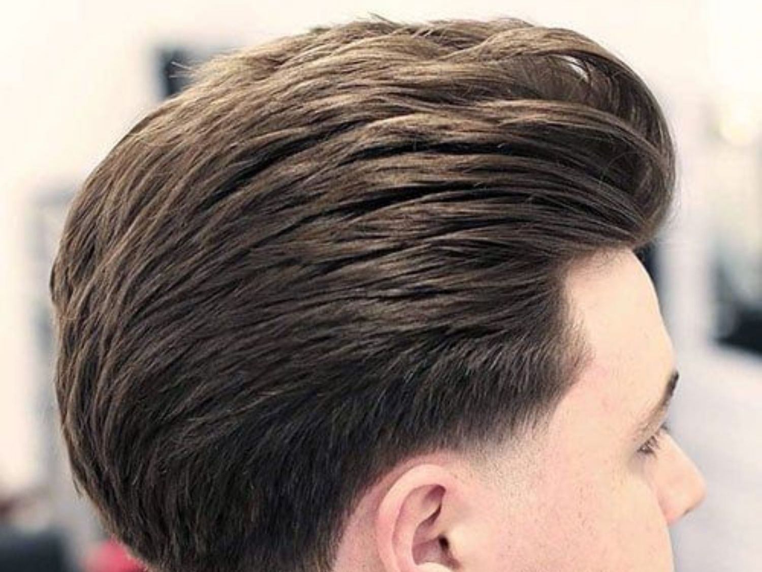 Close-up of a barber styling a precise fade haircut in a modern barbershop, emphasizing skill and detail.