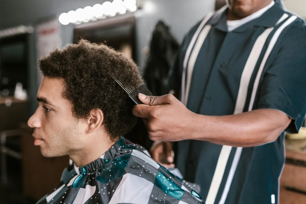 Professional barber giving a detailed haircut to a client with an Afro in a modern barbershop.