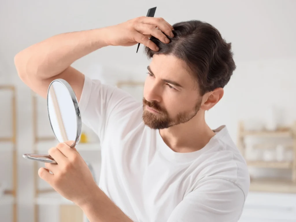 Man examining hair growth under men's toupee in Stafford, using comb and handheld mirror for natural look.
