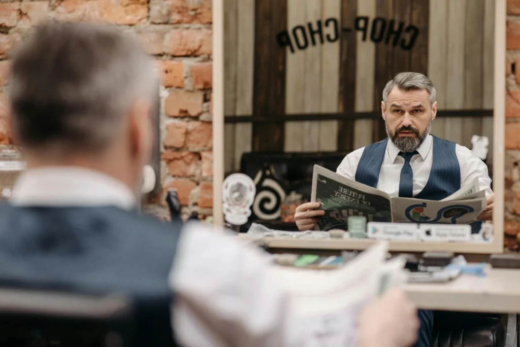 Barber blow-drying a man's large red beard and high-fade haircut in a bright, modern barbershop. Expert mens haircuts and grooming.