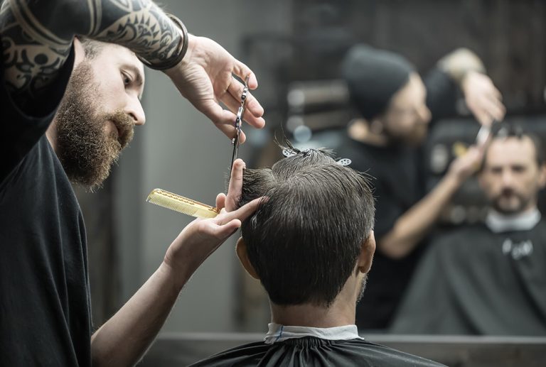 Professional barber giving a precise scissor haircut to a client inside a modern barber shop; focus on hand technique.