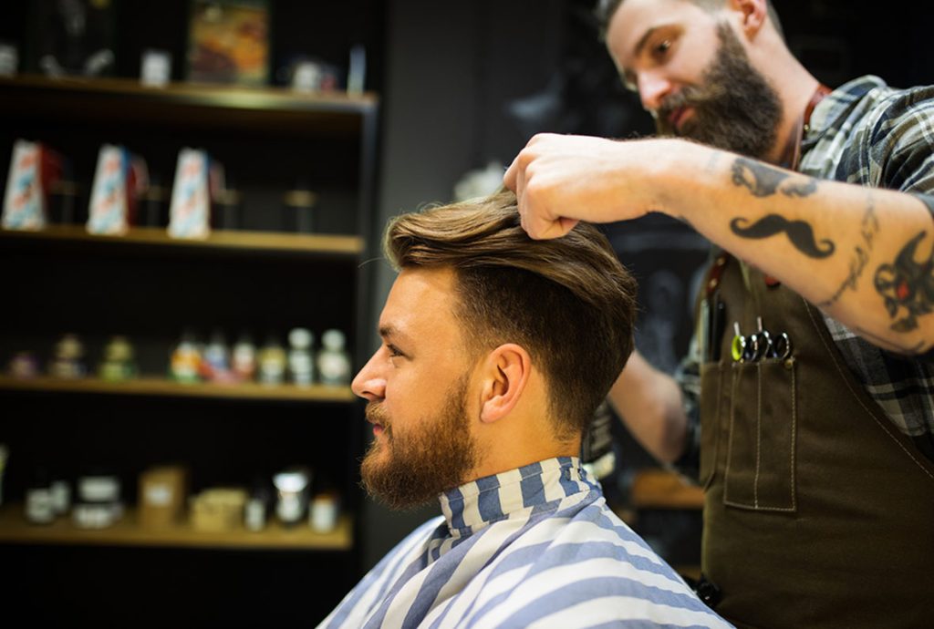 Client in striped cape receiving final touches on his modern hairstyle at the city's best barber shop.