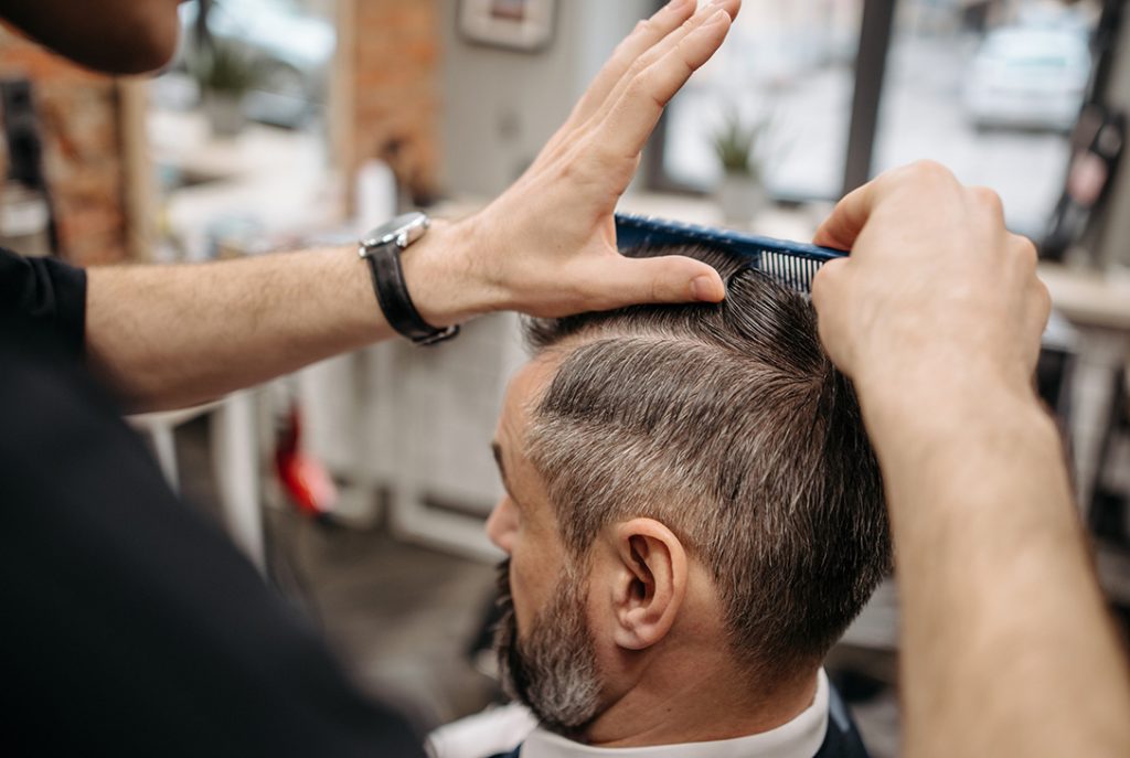 Barber combing and styling a distinguished, grey-haired client for premium services at cheap barber shops.