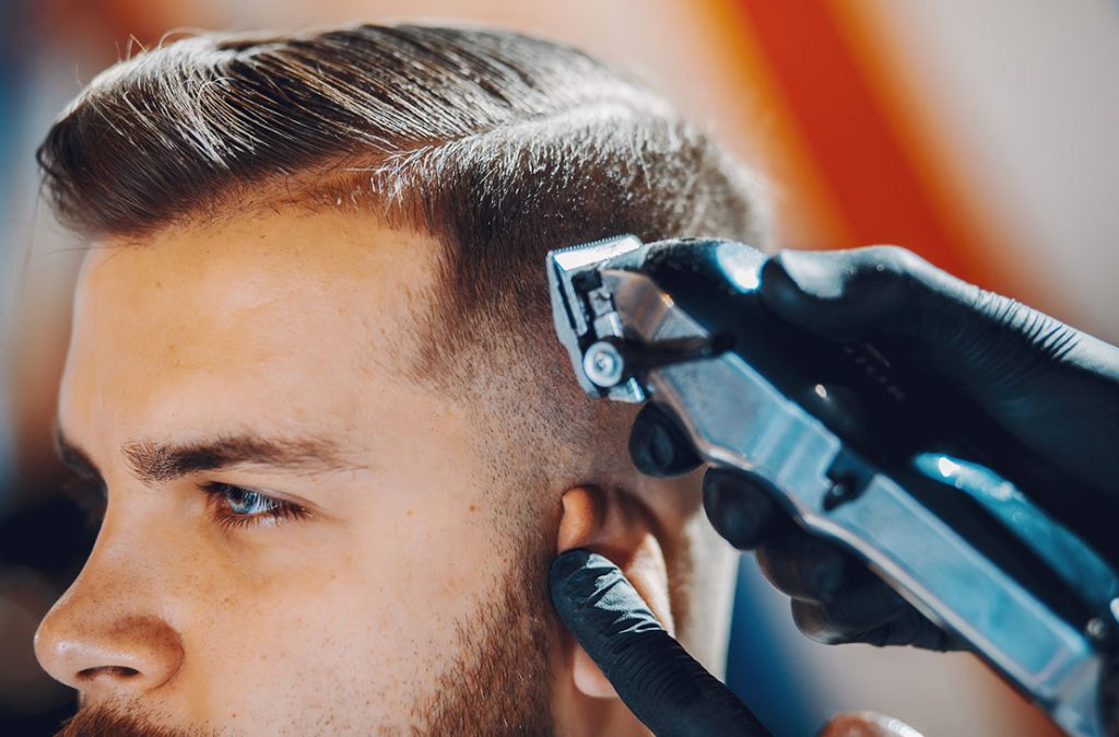 Close-up of a barber using an electric clipper to give a detailed low fade and trim. Find cheap barber shops near you.