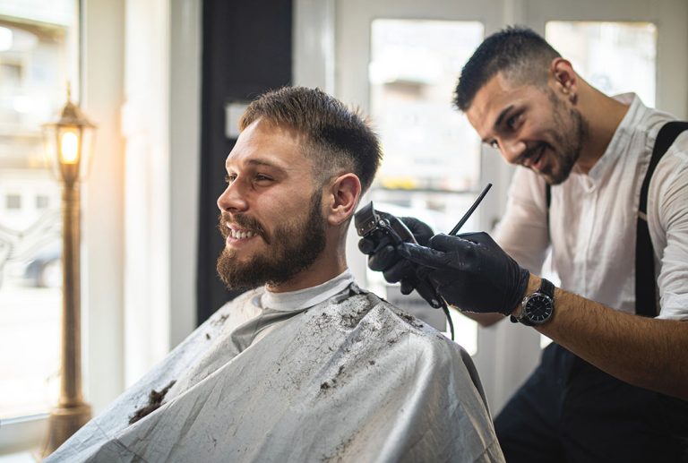 Smiling man getting a perfect side fade and beard trim from a barber in black gloves at one of the best cheap barber shops.